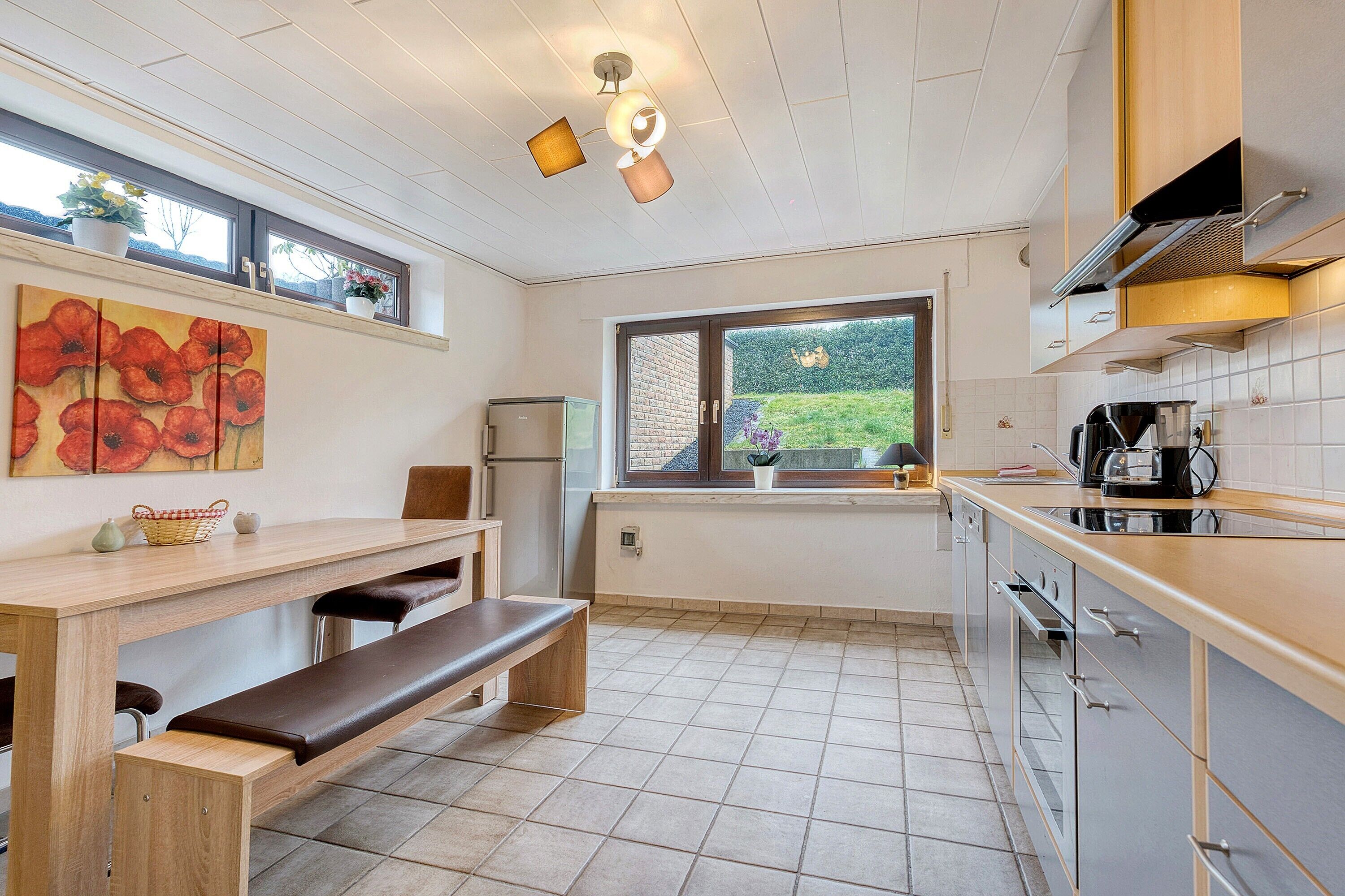 A modern kitchen with a bench, a refrigerator, a window with a view, and a painting on the wall.