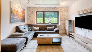 A living room with a sectional sofa, a coffee table, a TV, and a large window. - Holiday Apartment Am Linnert with Shared Terrace, Garden, and Wi-Fi (Haltern am See)