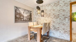 A dining area with a wooden table, chairs, a hanging light fixture, and a brick-patterned wall. - Holiday Apartment Am Linnert with Shared Terrace, Garden, and Wi-Fi (Haltern am See)