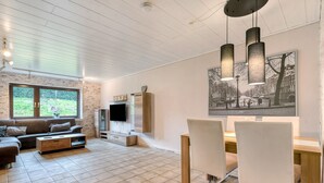 A modern living room with a sofa, TV, dining table, chairs, and artwork on the wall. - Holiday Apartment Am Linnert with Shared Terrace, Garden, and Wi-Fi (Haltern am See)