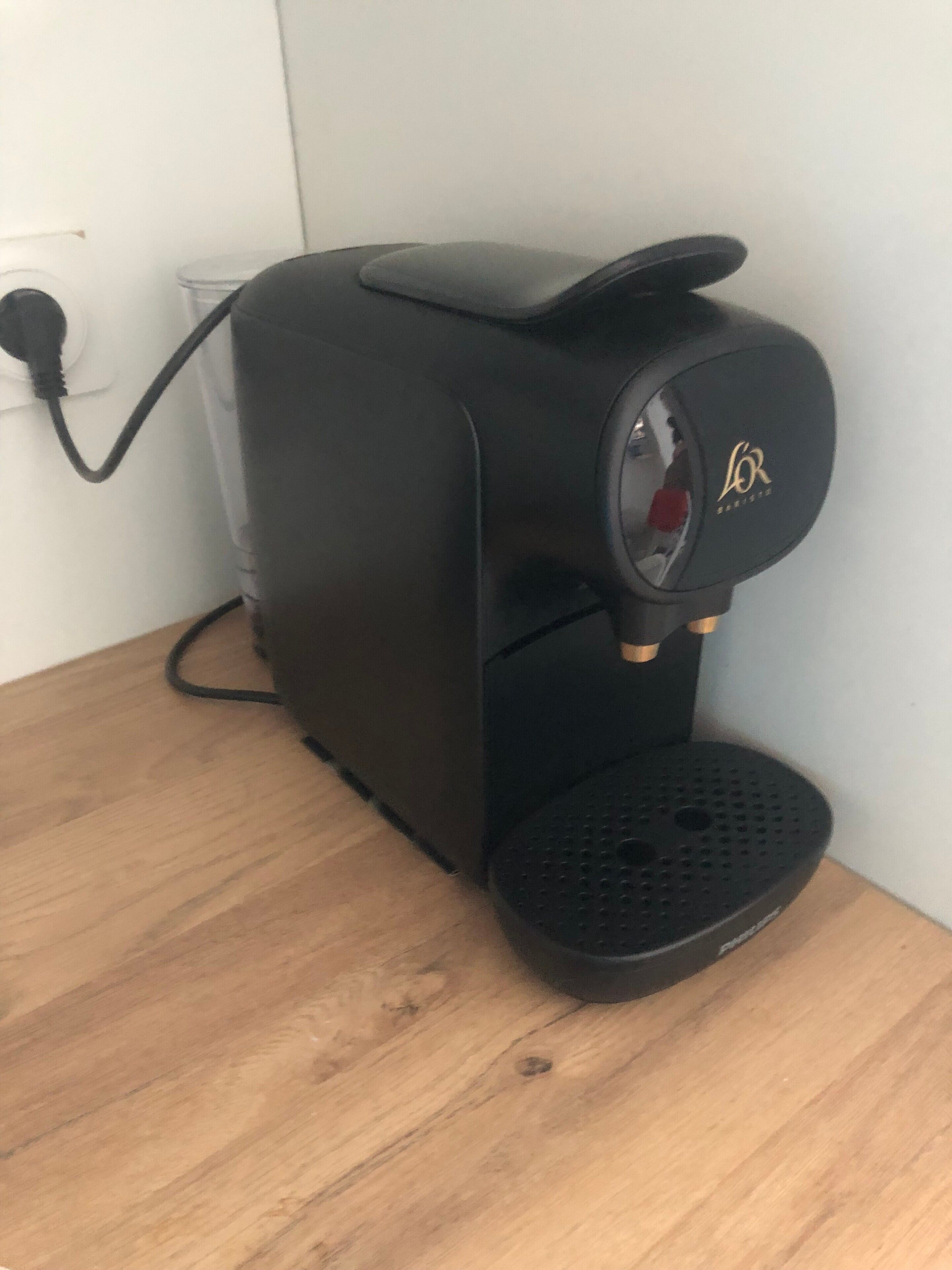 Une machine à café dotée d’un panneau de commande, d’un câble d’alimentation et d’un bac de récupération, posée sur une surface en bois.