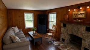 Un salon chaleureux avec une cheminée, des murs en bois, un canapé, un fauteuil à bascule et une table basse.