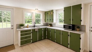 Une cuisine avec des meubles de couleur verte, un four à micro-ondes, un évier et des fenêtres donnant sur un paysage verdoyant.