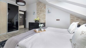 Ein modernes Schlafzimmer mit schrägem Dach, einem Bett mit weißer Bettwäsche, einer Kommode, einem Spiegel und einer Vase mit Blumen.