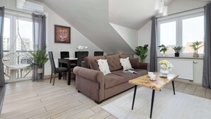 Ein modernes Wohnzimmer mit einem braunen Sofa, einem Holztisch und einem Essbereich mit einem weißen Tisch und Stühlen.