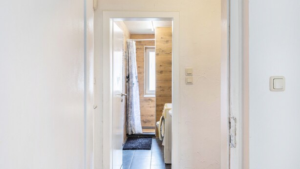 A narrow hallway with a door leading to a room with a washing machine. - Apartment 'Yellow F' (Miltenberg)