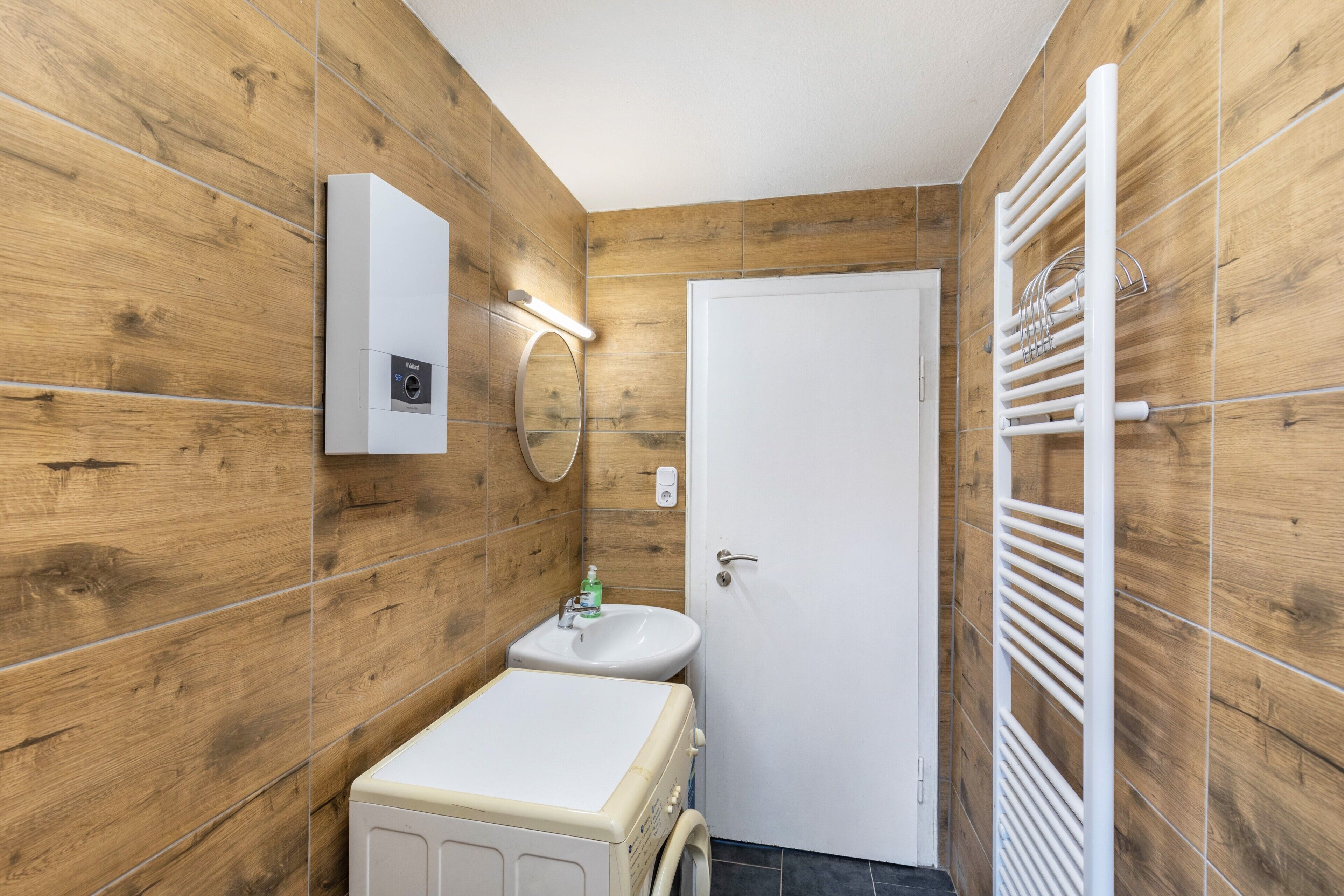 A compact bathroom with wooden walls, a white sink, a toilet, and a towel rack.
