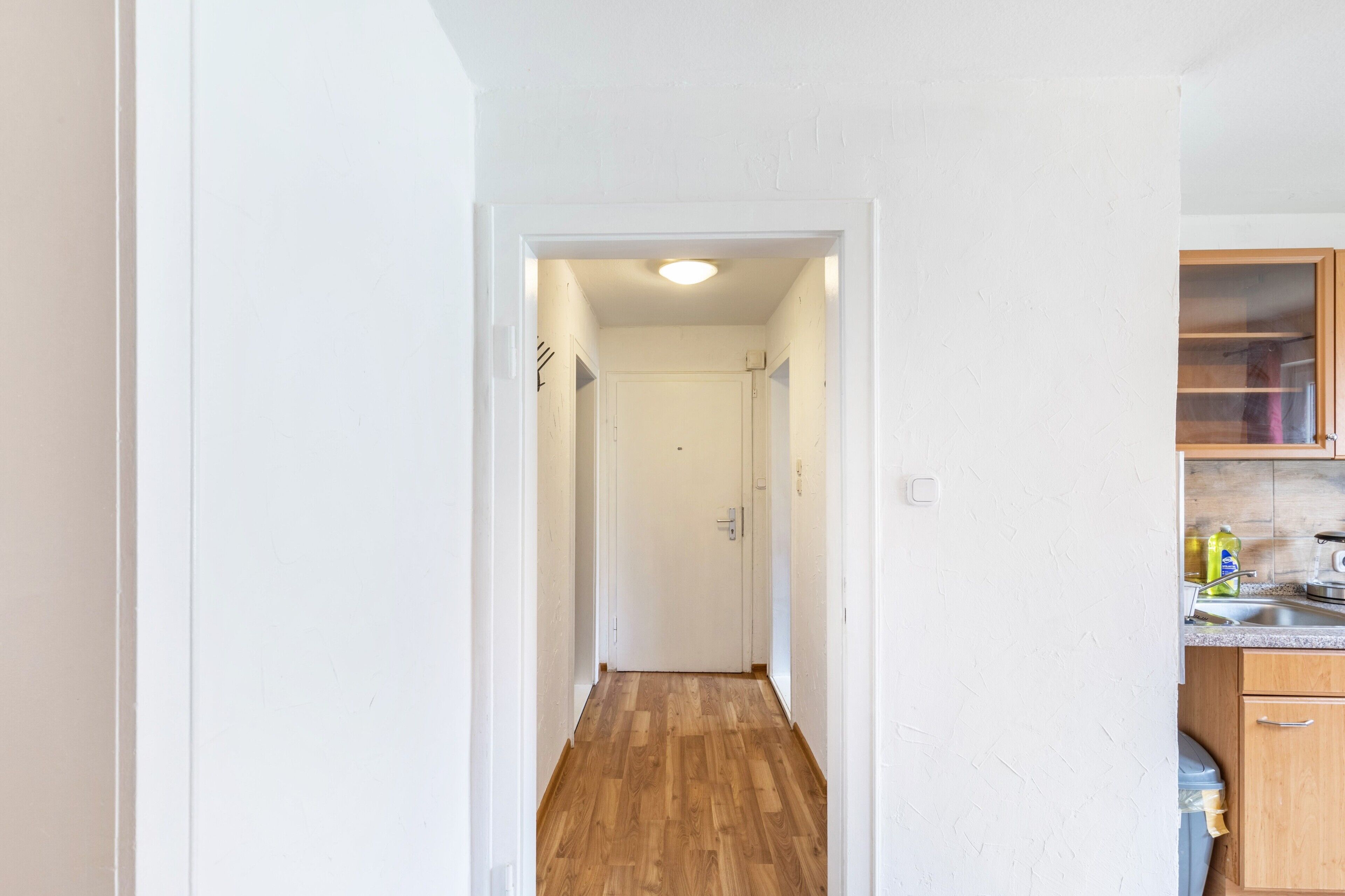 A narrow hallway with wooden flooring leading to a white door at the end.