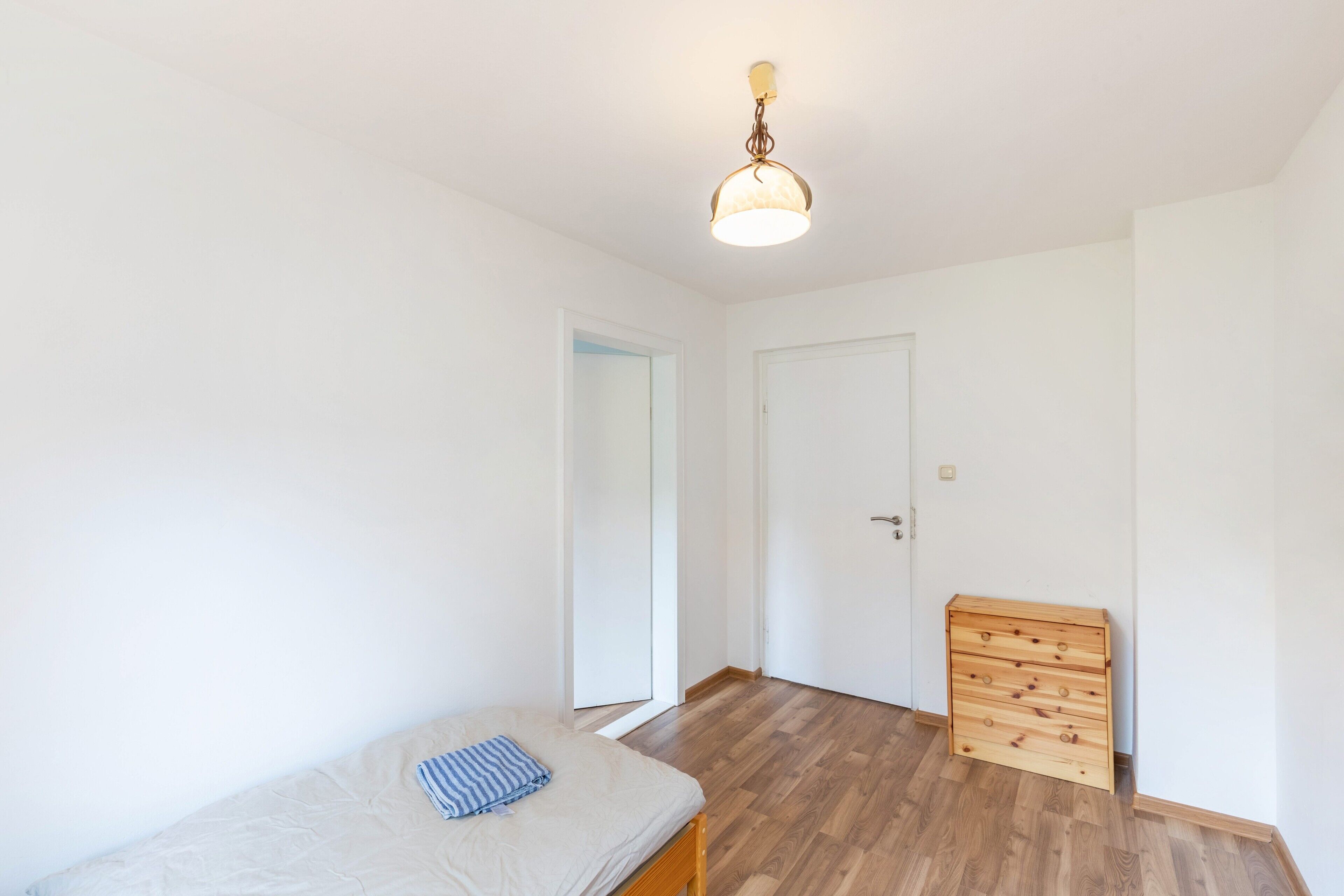 A bedroom with a bed, a wooden dresser, a door, and a light fixture.