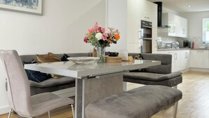 A modern kitchen with white cabinets, a dining table with grey upholstered chairs, and a vase of flowers on the table. - The Kipling Inn, 4 - Bed, Sleeps 6, Long Term Rental Available (Ulverston)