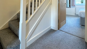 A staircase with white railings leading to a bedroom with a wooden door and a window with curtains. - The Kipling Inn, 4 - Bed, Sleeps 6, Long Term Rental Available (Ulverston)