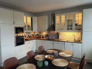 Une cuisine moderne avec des meubles blancs, un four encastré et un coin repas comprenant une table noire et des sets de table en fibres tressées.