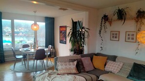 A cozy living room with a sofa, a coffee table, and a dining area with chairs and a table. There are plants and a poster on the wall. - Cozy house 600 meters from the city center, view of the water and beautiful nature (Halmstad)