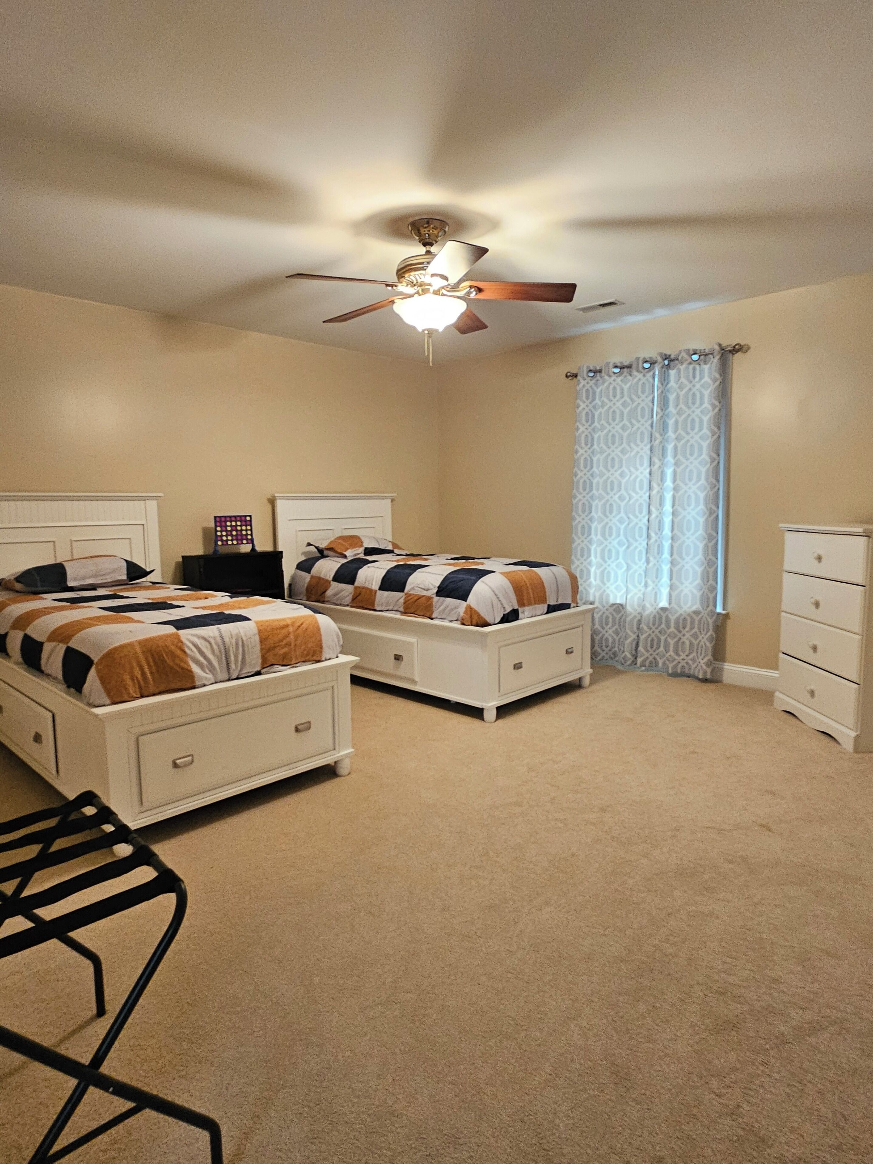 Een slaapkamer met twee bedden, een plafondventilator, een raam met decoratieve gordijnen en een dressoir.