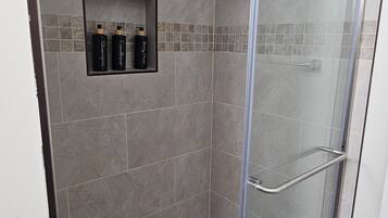 A shower with a glass door, a tiled wall, and a shelf with toiletries.