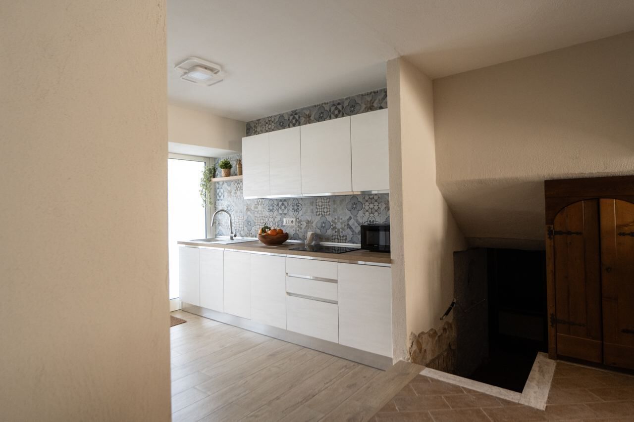 A modern kitchen with white cabinets, a tiled backsplash, and a wooden door.