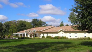 A row of single-story buildings with a tiled roof, surrounded by a grassy field and trees. - AU P'TIT CREUX DES LANDES (Ychoux)