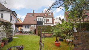 En privat trädgård med krukväxter, en träbänk och ett hus med ett tak täckt av takpannor.
