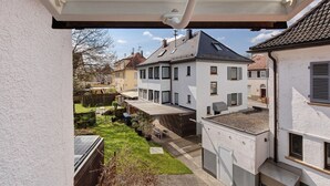 En bostadsbyggnad med ett sluttande tak, en synlig skorsten och en liten trädgårdsyta med en bänk och planterade blommor i krukor.