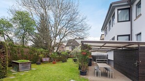 Een achtertuin met terras, plantenpotten en een houten schutting.