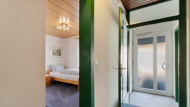 Een kamer met een bed, een klein nachtkastje, een lijst met een afbeelding aan de muur, en een deur naar een balkon.