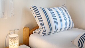 Een bed met een gestreept kussen, een nachtkastje met een lamp en een stopcontact.