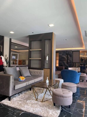 A modern hotel lobby with a grey sofa, a blue armchair, and a marble floor.