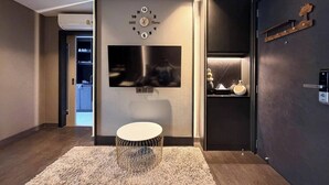 A modern living room with a flat-screen TV mounted on the wall, a round coffee table, and a dark-colored sofa. - Room-luxury Condo, Chaing Mai Night Baza (Chiang Mai)