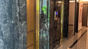 A hallway with marble walls and a polished floor, leading to an elevator and a door with a sign. - Room-luxury Condo, Chaing Mai Night Baza (Chiang Mai)