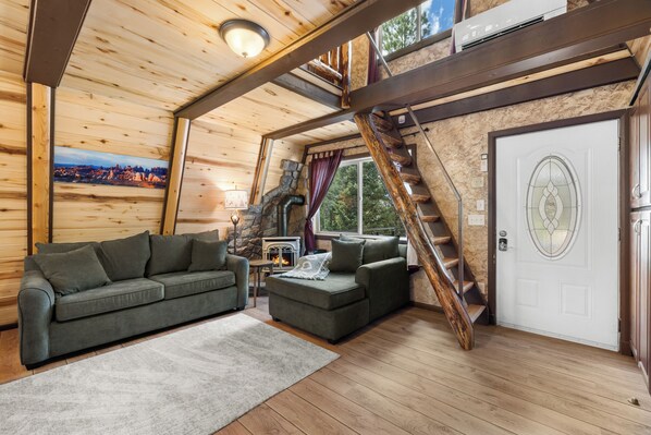 A cozy cabin interior with a wooden ceiling, a stone fireplace, a sofa, a staircase, and a door with a decorative glass panel. - Zion's Emerald| Walk into East Zion| Amazing Stars (Orderville)