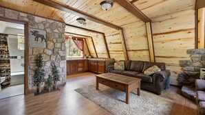 Ein gemütliches Blockhaus-Interieur mit einer Steinwand, Holzbalkendecke, Kamin, Sofa und Couchtisch.
