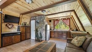 Ein gemütliches Blockhaus-Interieur mit Steinwand, Holzbalkendecke, einer herzförmigen Dekoration, einem montierten Fernseher und einem Kamin aus Stein.