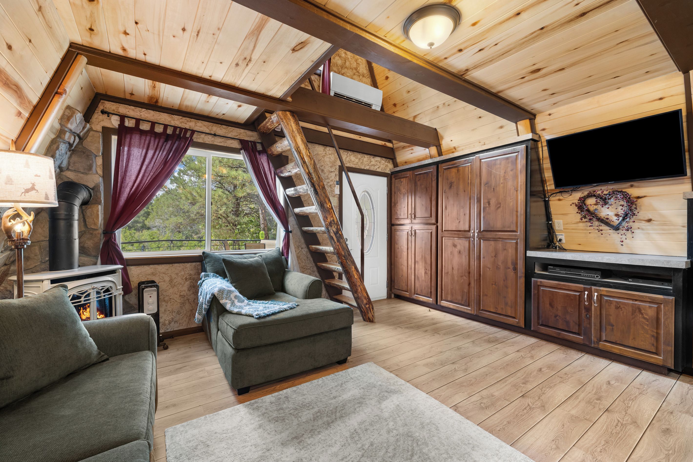 Interior acolhedor de uma cabana com lareira, um sofá, uma televisão e armários de madeira.