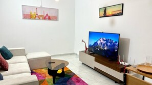 Ein modernes Wohnzimmer mit einer Couch, einem Couchtisch, einem Fernseher auf einem Holzgestell und einem farbenfrohen Teppich.