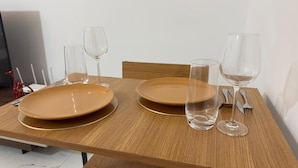 Een houten eettafel met twee bruine borden en twee wijnglazen.