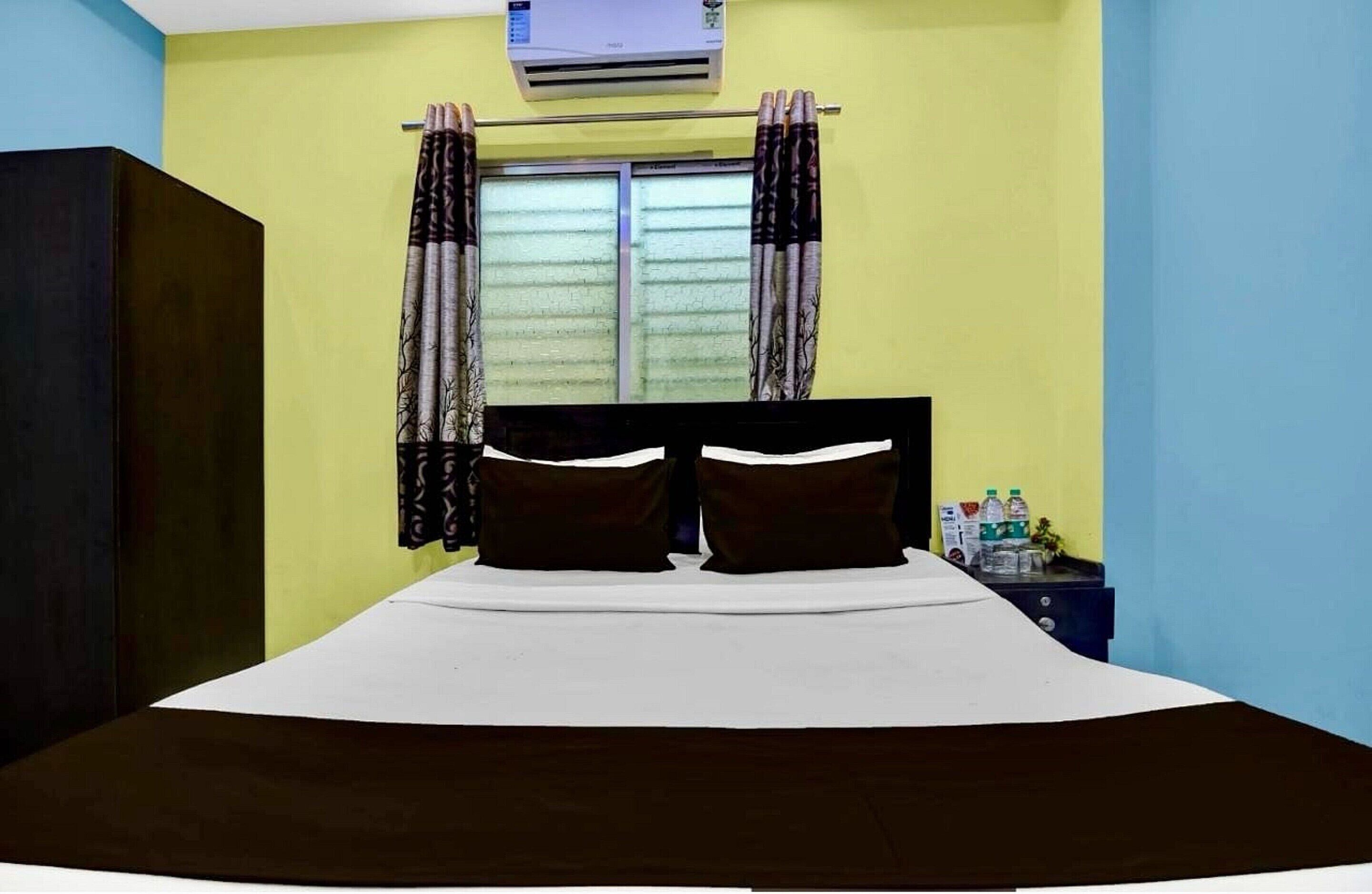 A bedroom with a bed, curtains, an air conditioning unit, and a nightstand with items.