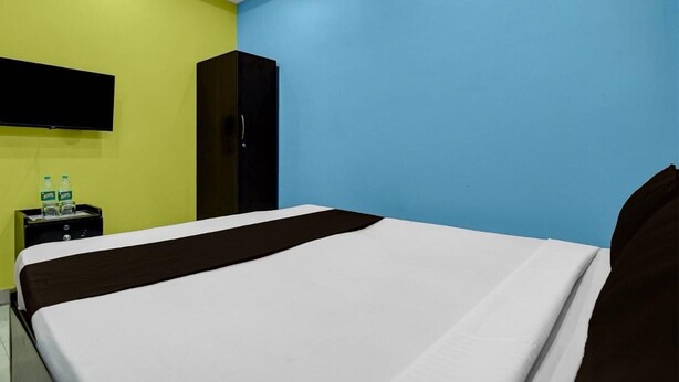 A hotel room with a bed, a TV mounted on the wall, a wardrobe, and a nightstand with water bottles. - Hotel O Metropolis Mall Kolkata (Barasat)
