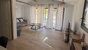 Tilava olohuone, jossa on puulattia, pyöreä sohvapöytä, harmaa sohva ja televisio puuraisella jalustalla.