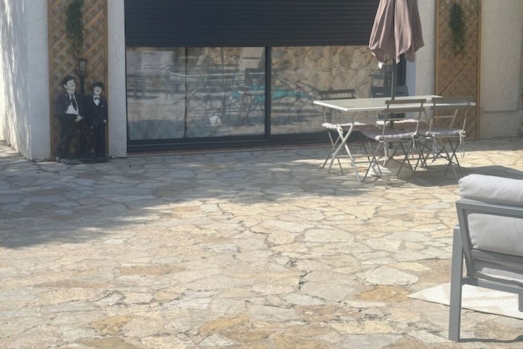 An outdoor patio area with stone flooring, a table with chairs, and a large window with a view of the street.