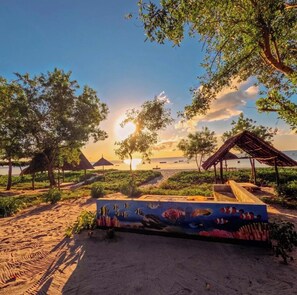 A beach scene with a wooden bench, thatched-roof structures, and a painted mural of marine life. - MAISARA MAFIA BEACH LODGE (Mafia Island)