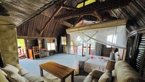 Ein geräumiges Zimmer mit hoher, hölzerner Decke, einem großen Bett mit Baldachin, einem Holztisch und zwei Sofas.