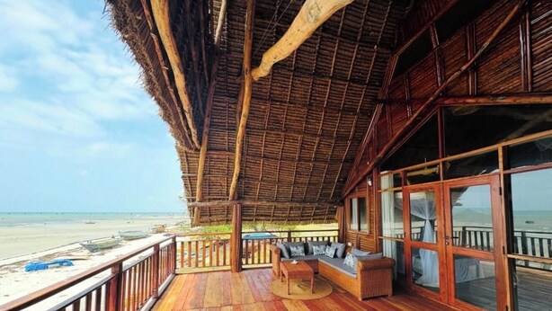 Eine Holzterrasse mit einem Reetdach mit Blick auf einen Strand.