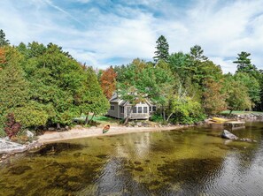 Una cabaña junto a un lago tranquilo rodeada de árboles frondosos.