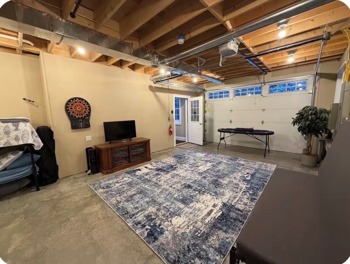 A basement with a large rug, a dartboard, a television, and a garage door.