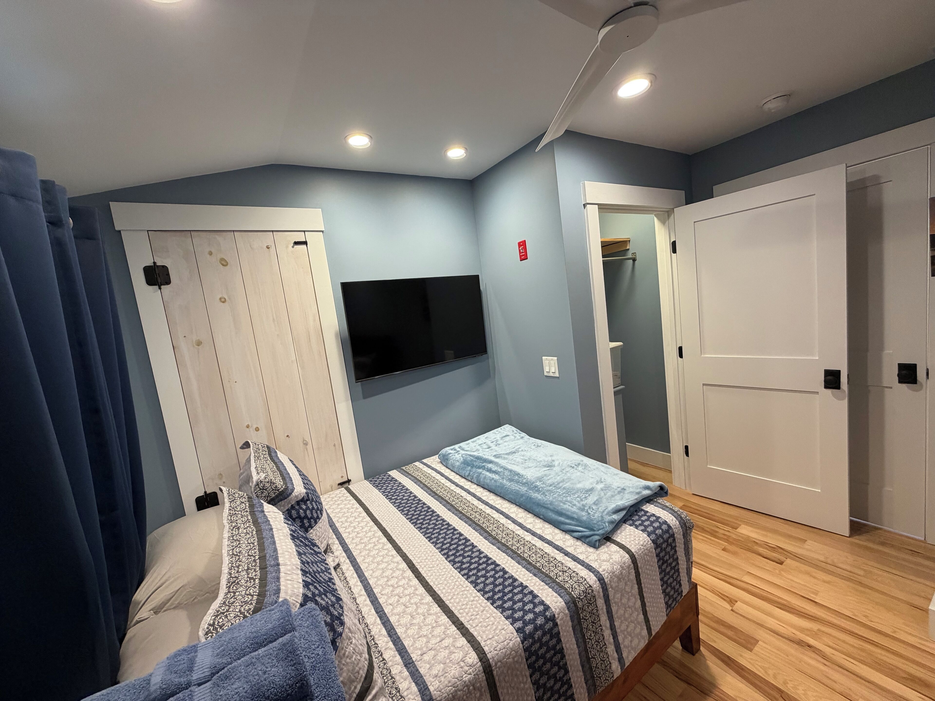 A bedroom with a bed, a TV mounted on the wall, a wardrobe, and a door leading to a closet.
