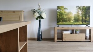 Una sala de estar moderna con un escritorio de madera, un florero y un televisor de pantalla plana sobre un soporte de madera.