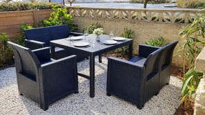 Un área de comedor al aire libre con mobiliario de mimbre, una mesa dispuesta para cuatro personas y vistas a un río y edificios al fondo.