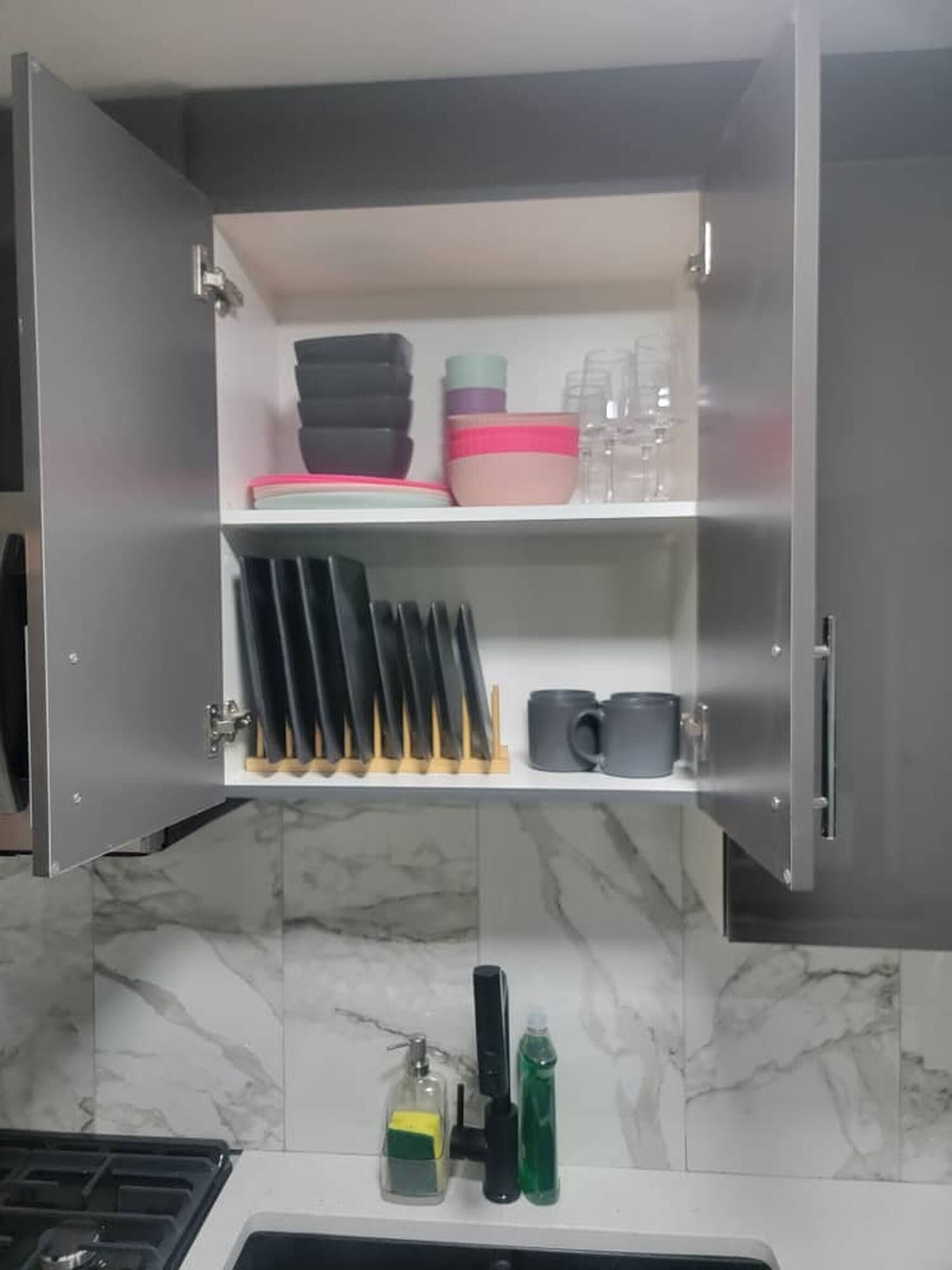 A kitchen with a marble backsplash, a stainless steel cabinet with utensils, plates, and mugs.