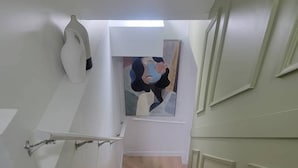 Una escalera con detalles en madera clara, paredes blancas y un cuadro en la parte superior.