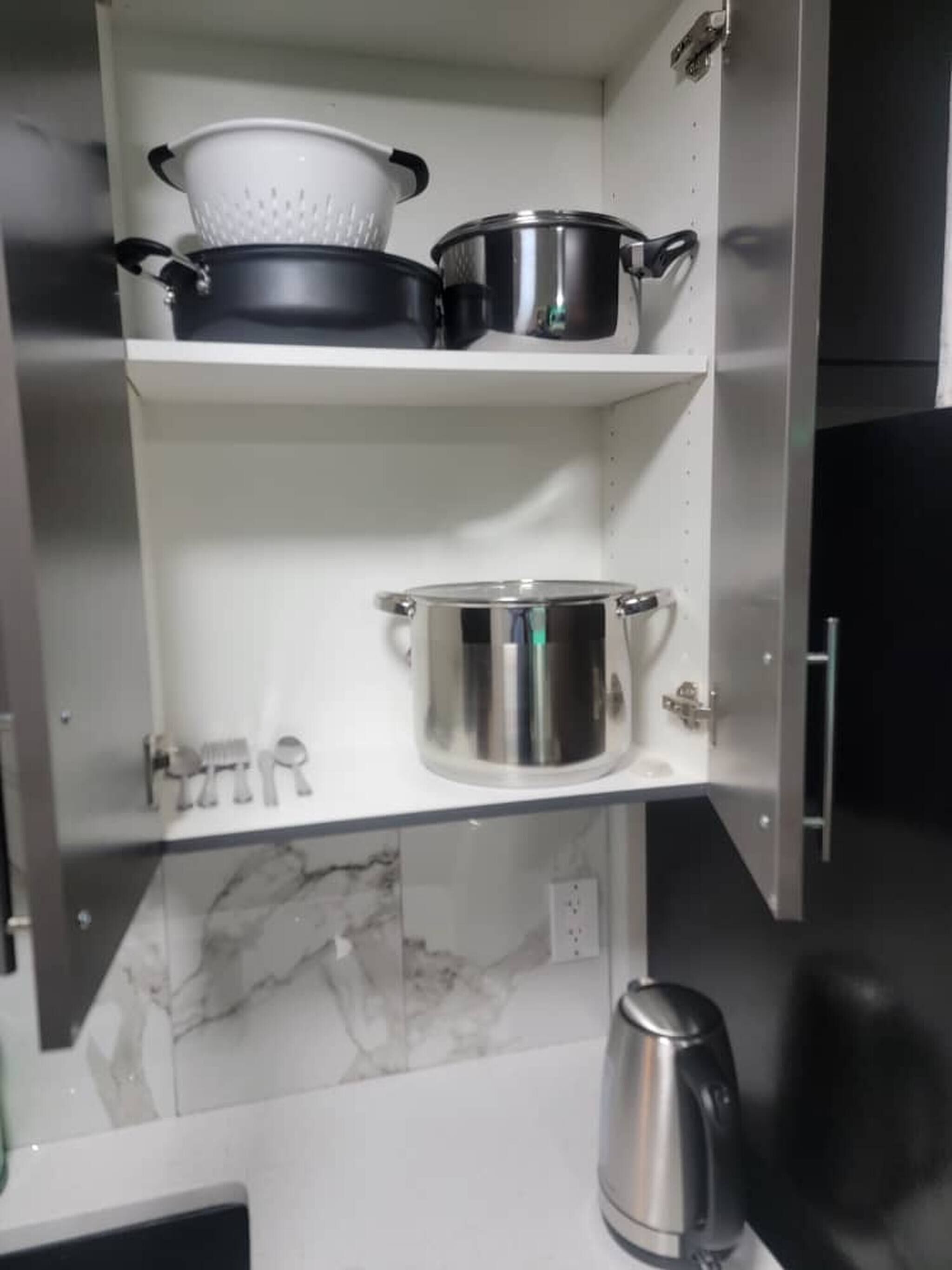 A kitchen with stainless steel pots and a kettle on shelves, a marble backsplash, and a black refrigerator.